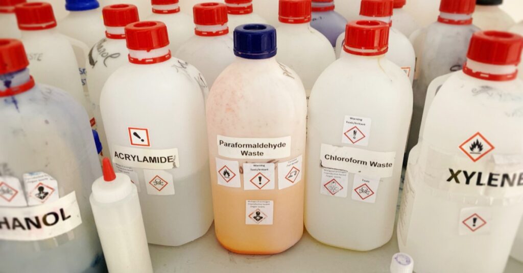 Several solvent bottles with blue and red caps are sitting on a table. Labels and caution signs are on each bottle.