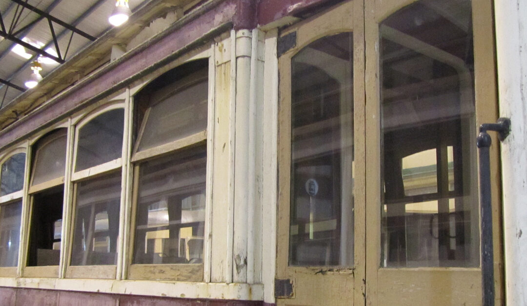 An old train car is in a restoration facility. The train car is red and brown with white trimming near the windows.