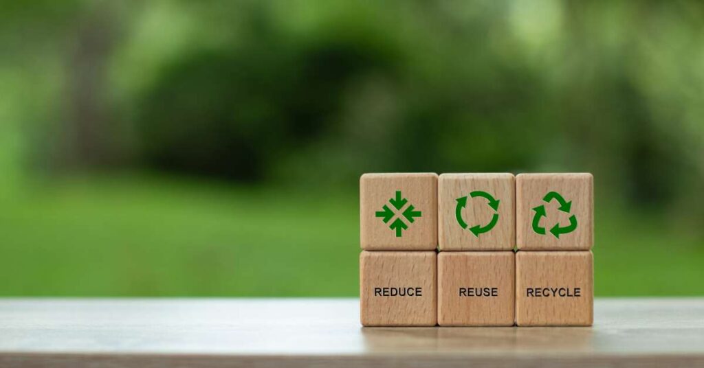 The words “reduce," "reuse," and "recycle” and symbols are on wooden blocks. The symbols are green and the words are black.