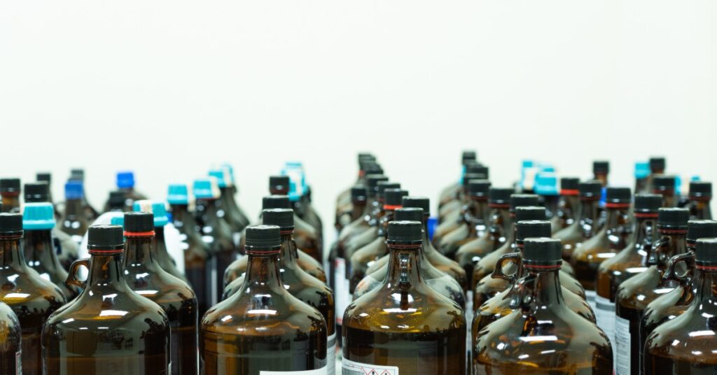 Several chemical bottles are lined up. They are dark brown with black caps, while the bottles in the back have blue caps.