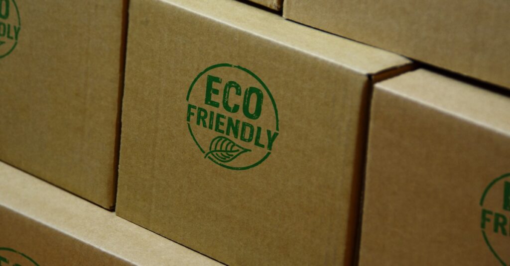 A close-up of one box among a pile of boxes that have an "Eco Friendly" stamp. The stamp is green and the boxes are brown.