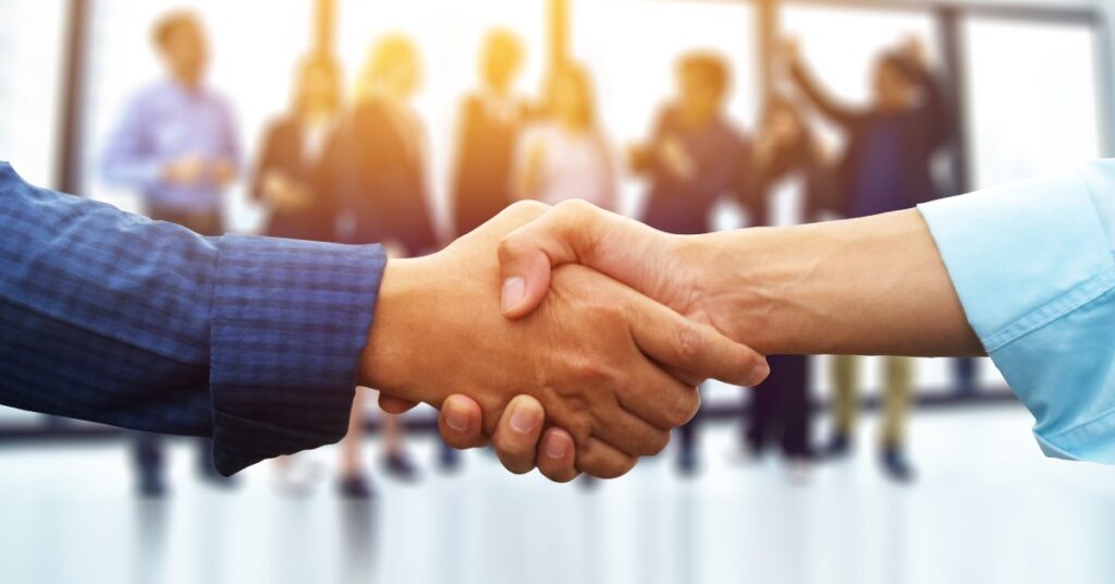 A close-up of two people shaking hands. One person is wearing a blue plaid shirt and the other has a solid blue shirt.