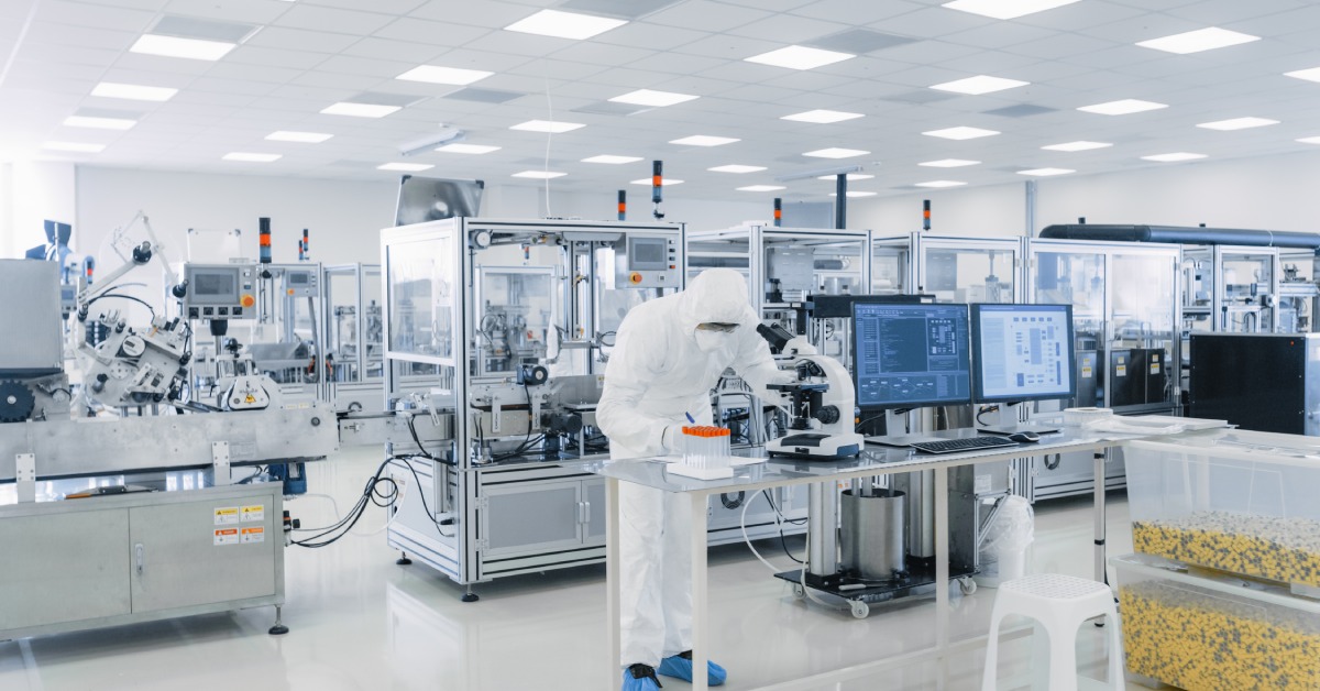 A laboratory with several machines. A person stands at a table with a microscope and writes on a piece of paper.