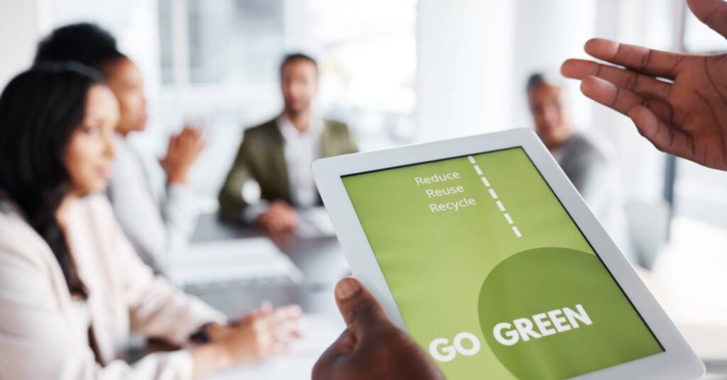 Close-up of someone holding a tablet that says, "Go Green" and "Reduce, Reuse, Recycle." People are in the background.