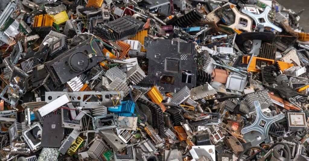 A large pile of electronic waste in a scrap yard. The waste includes circuit boards, coils, wires, and more.