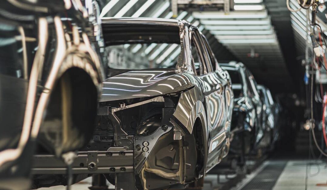 A vehicle production line in an automotive manufacturing plant. The vehicles are grey and don't have a front bumper.