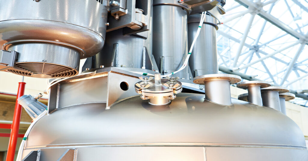 Close-up of large stainless steel dissolver vessel with industrial piping in modern manufacturing facility.