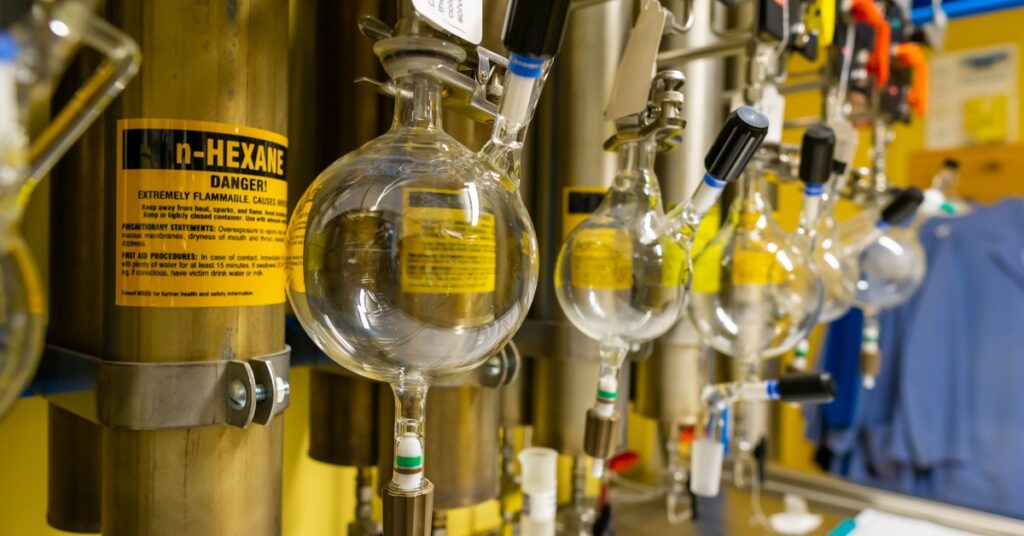 A row of round-bottom flasks containing clear solvent hanging from a distillation unit in a yellow lab.