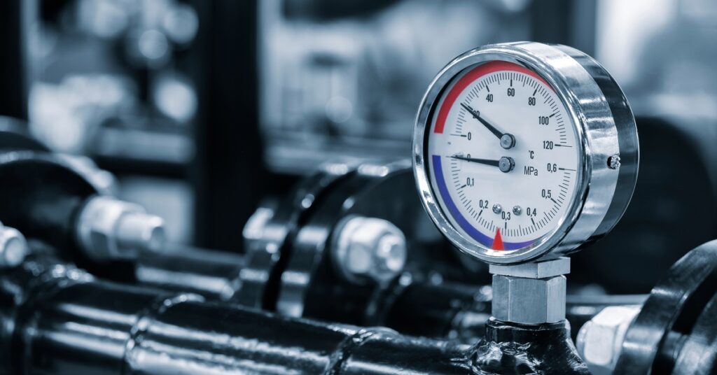 A dark pipe with a circular dial gauge showing pressure and temperature readings in an industrial setting.