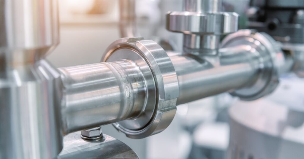 A close-up of polished metal piping with flanges and valves mounted on a shiny processing machine base.