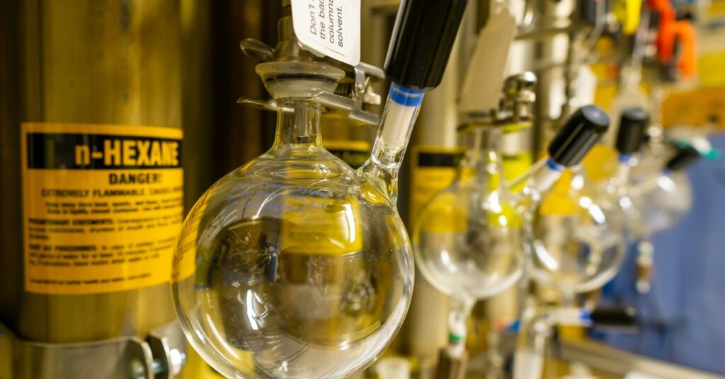Glass flasks hanging from metal fittings beside labeled hexane cylinders and lab equipment.