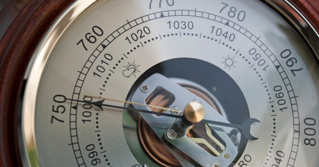 A close-up of a barometer dial with a metallic pointer indicating pressure and weather symbols across the face.