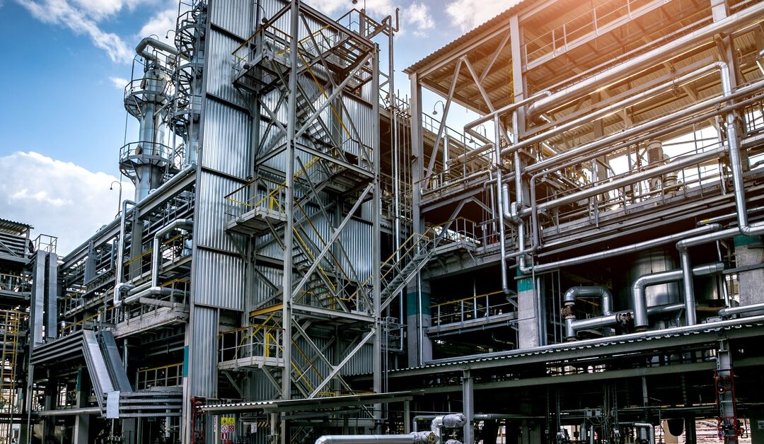 An industrial facility with extensive metal piping, walkways, and steel structures under a partly cloudy sky.