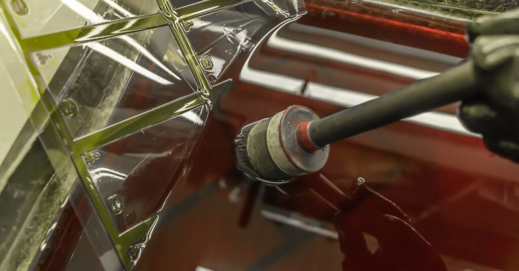 A gloved worker holding a rotary brush over a liquid bath filled with submerged metallic aircraft parts.