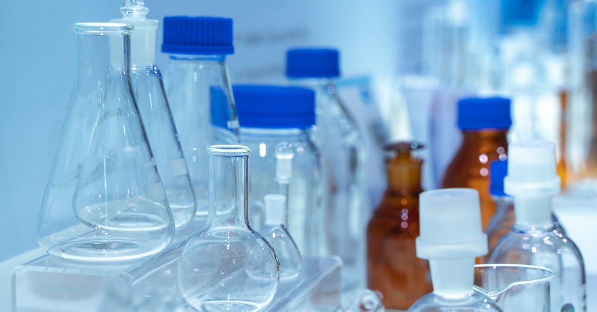 Assorted laboratory glassware and plastic bottles with blue caps arranged on a clean bench in a bright lab.