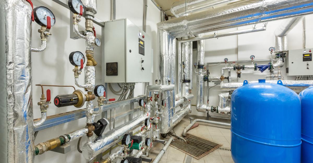 A complex system of insulated industrial pipes, valves, and gauges connected to large blue storage tanks.