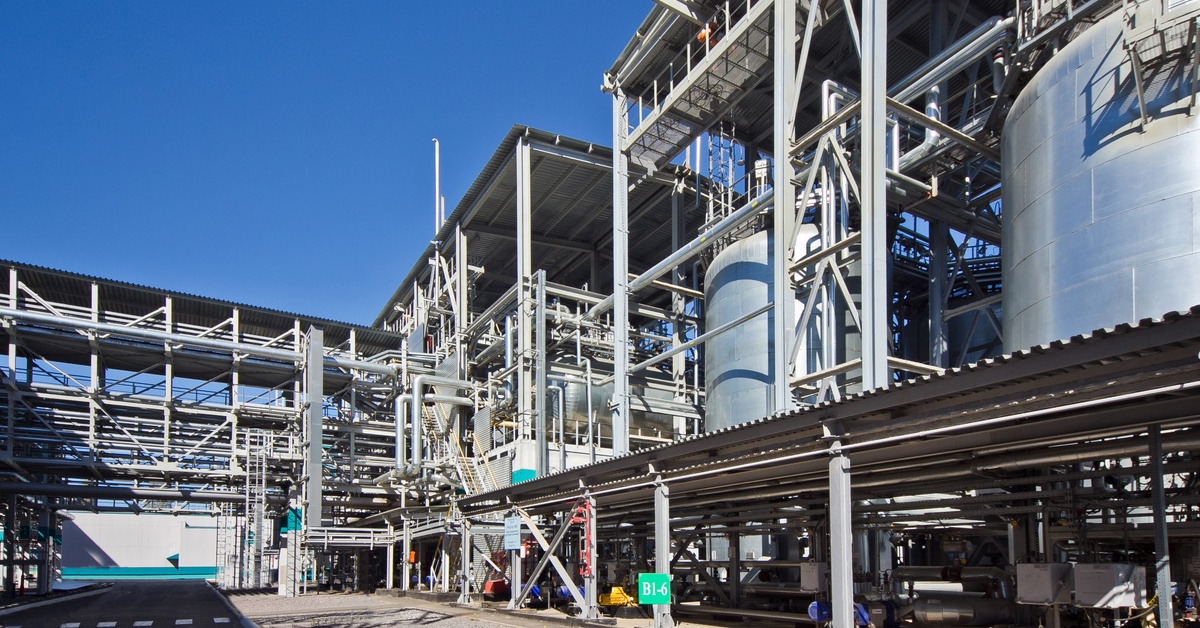 The outside view of an industrial factory that contains large, silver storage systems and a complex pipe system.