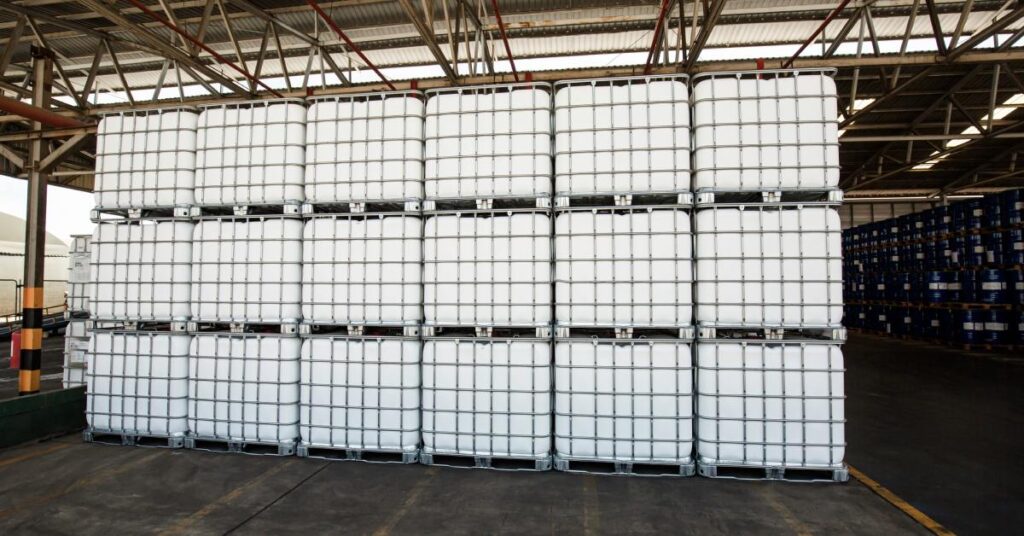 A stack of white, plastic containers in metal cages are stacked up three high in an open warehouse.