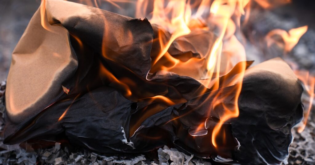 A close-up view shows something being incinerated by a small fire. It sits on a pile of gray and black ash.