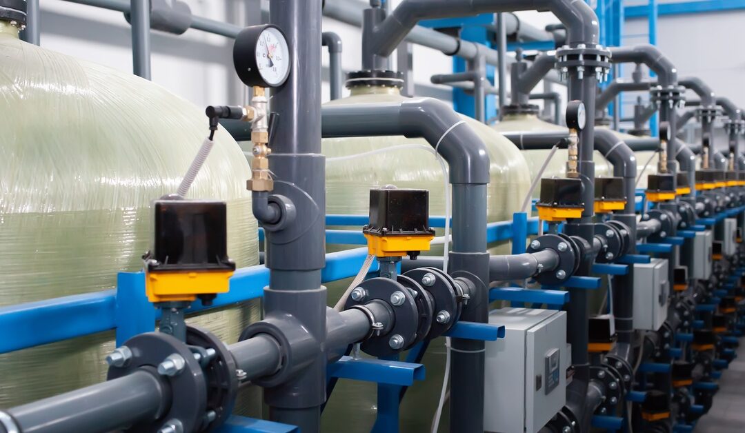 Several large industrial containers are linked with large dark-gray pipes. Each container has a pressure gauge attached.