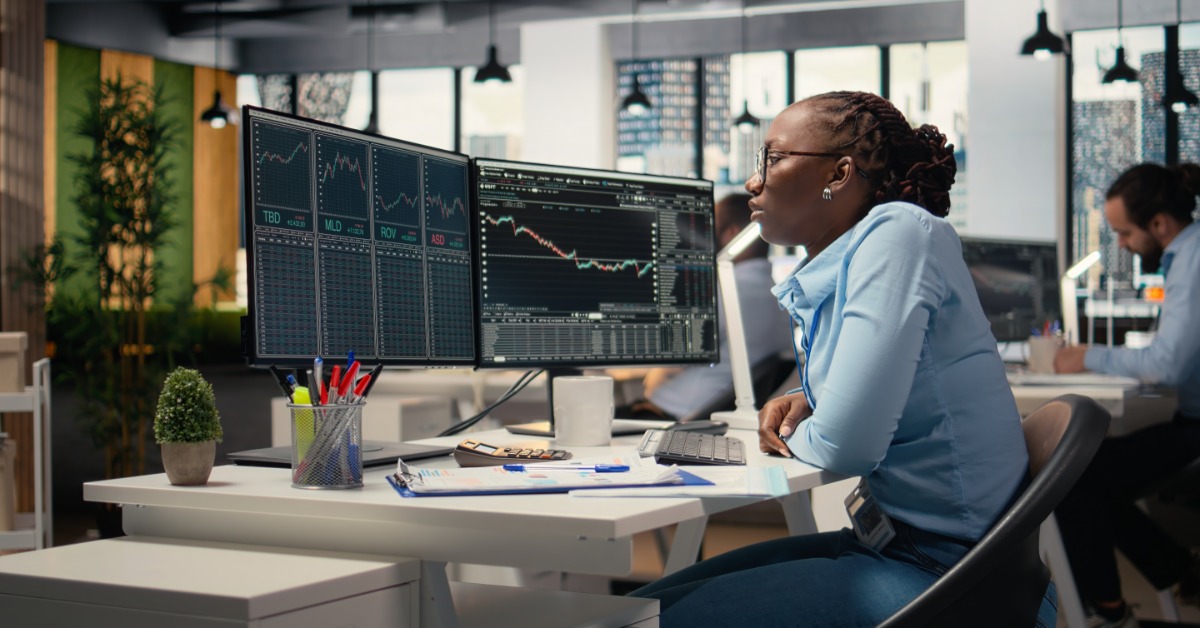 A woman stands at the head of a conference room giving a presentation to three people sitting at the table.