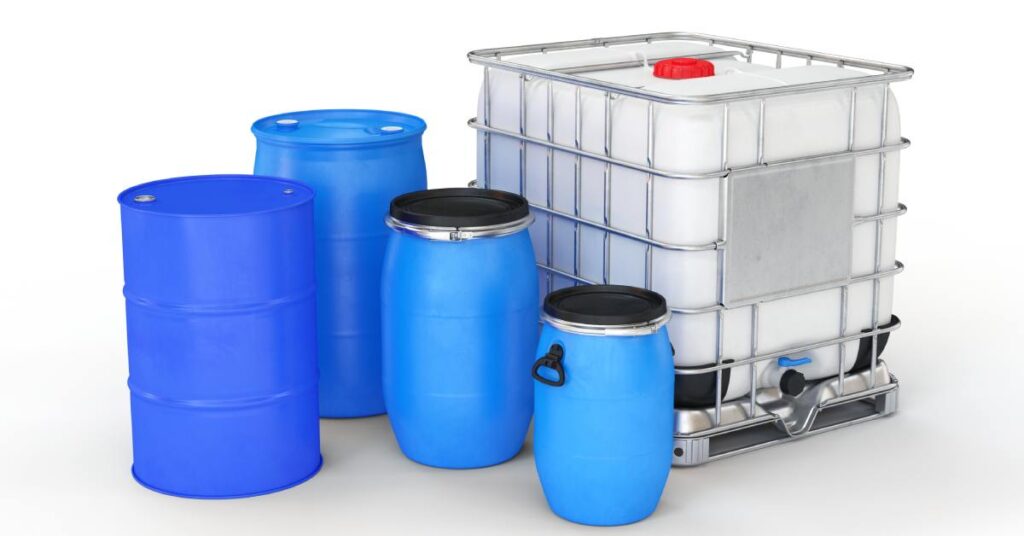 Five different industrial plastic drums sit empty together. Four of them are blue, and one is white.