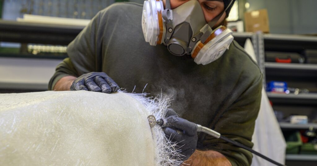 A close-up view shows a person wearing a respirator mask using a Dremel to trim a piece of fiberglass.
