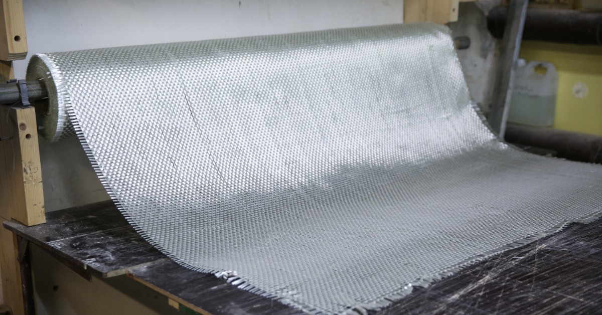 White fiberglass fabric is being pulled off it's spool and draping across a table in a factory.