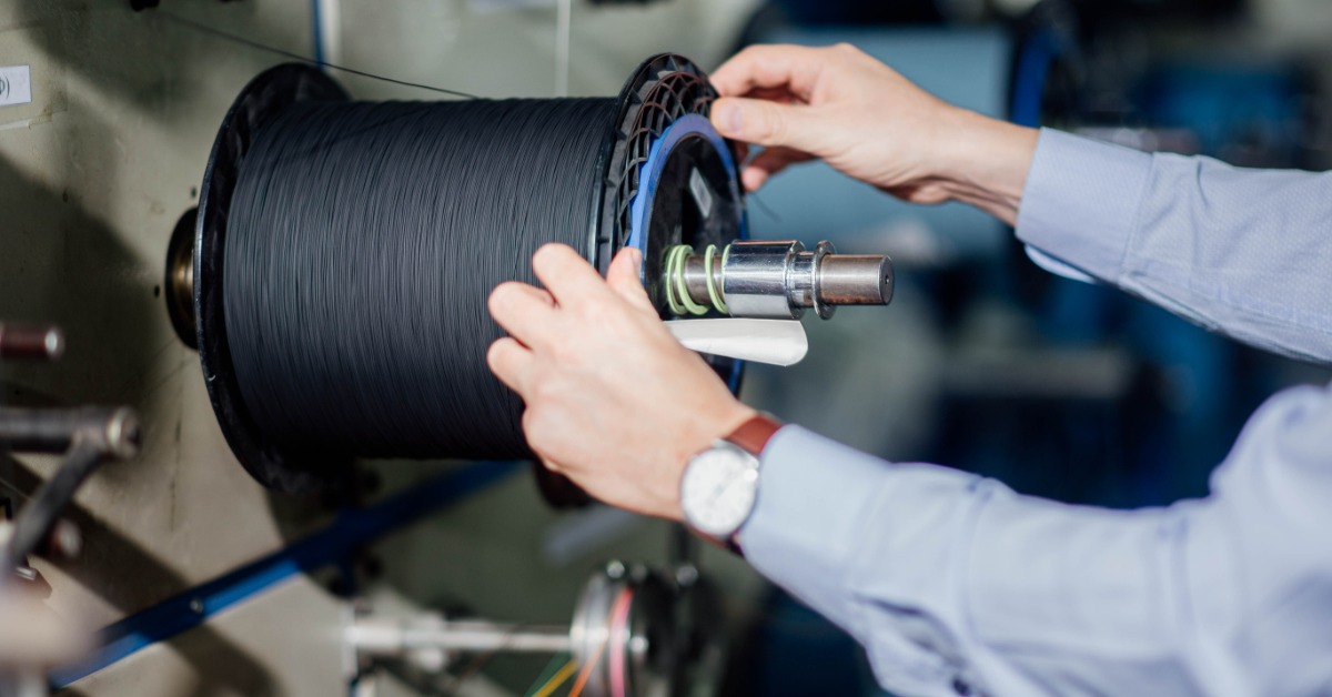 A close-up view shows a person's hands holding onto the plastic end of a spool that contains black fiberglass.