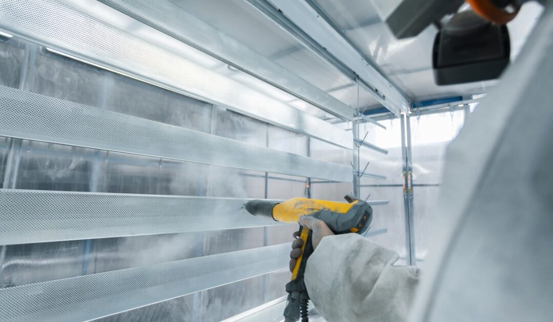 A person wearing a white protective suit and a face mask is using a yellow industrial sprayer to paint.