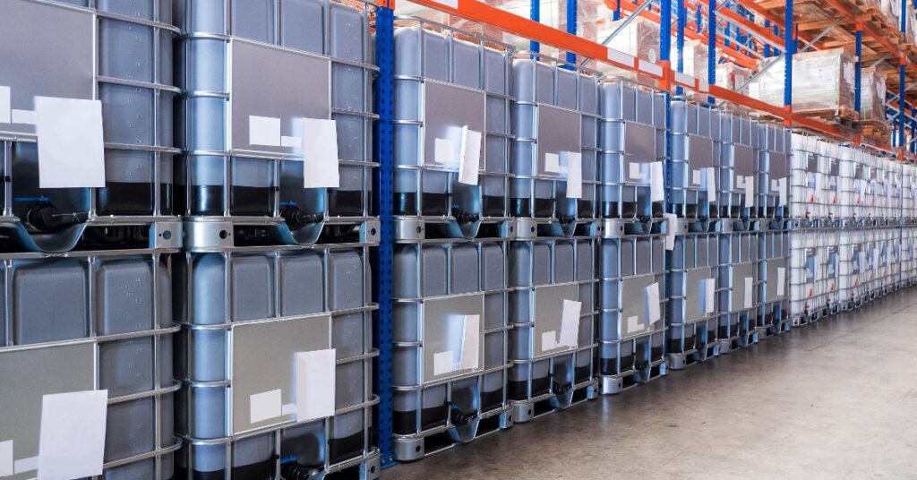 Large dark-gray and white containers are in long rows and stacked on top of each other in a warehouse.