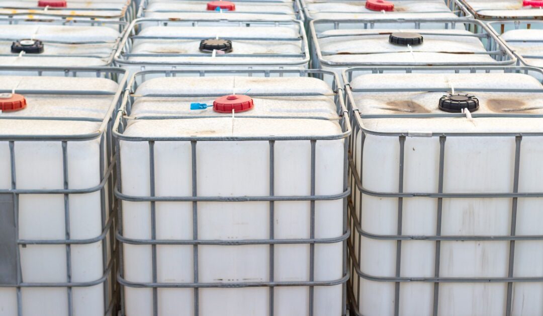 Three rows of white, square containers sit outside on a concrete surface. Metal bars surround the containers.